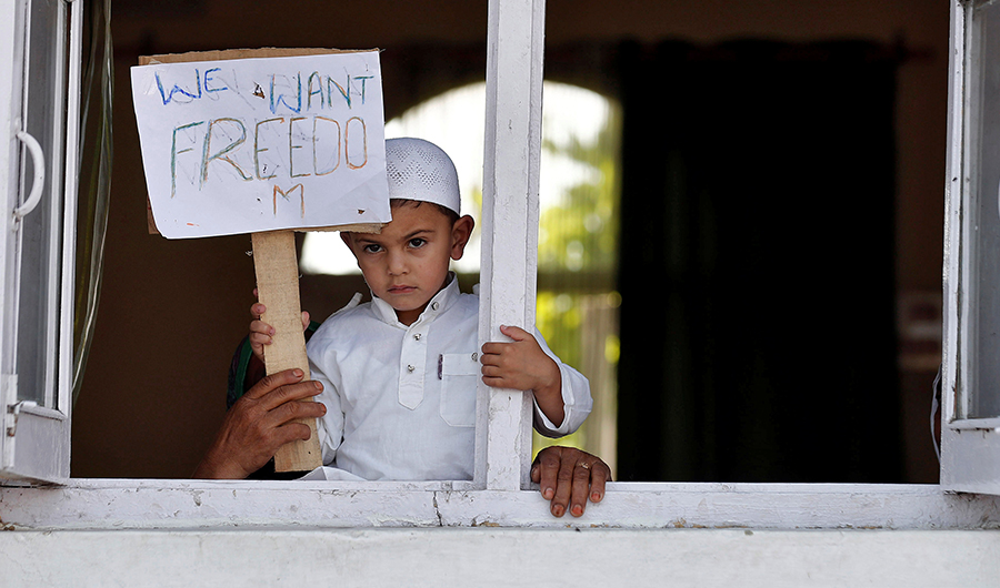 A Kashmiri boy displays a placard from a window at a protest site after Friday prayers during restrictions, after scrapping of the special constitutional status for Kashmir by the Indian government, in Srinagar, August 23, 2019. (REUTERS)
