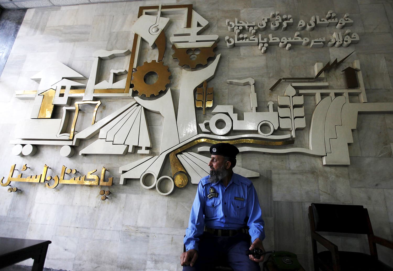 A security guard sits in front of a wall with signs and slogans at the operation building at the Pakistan Steel Mills (PSM) on the outskirts of Karachi Feb 8, 2016.—Reuters