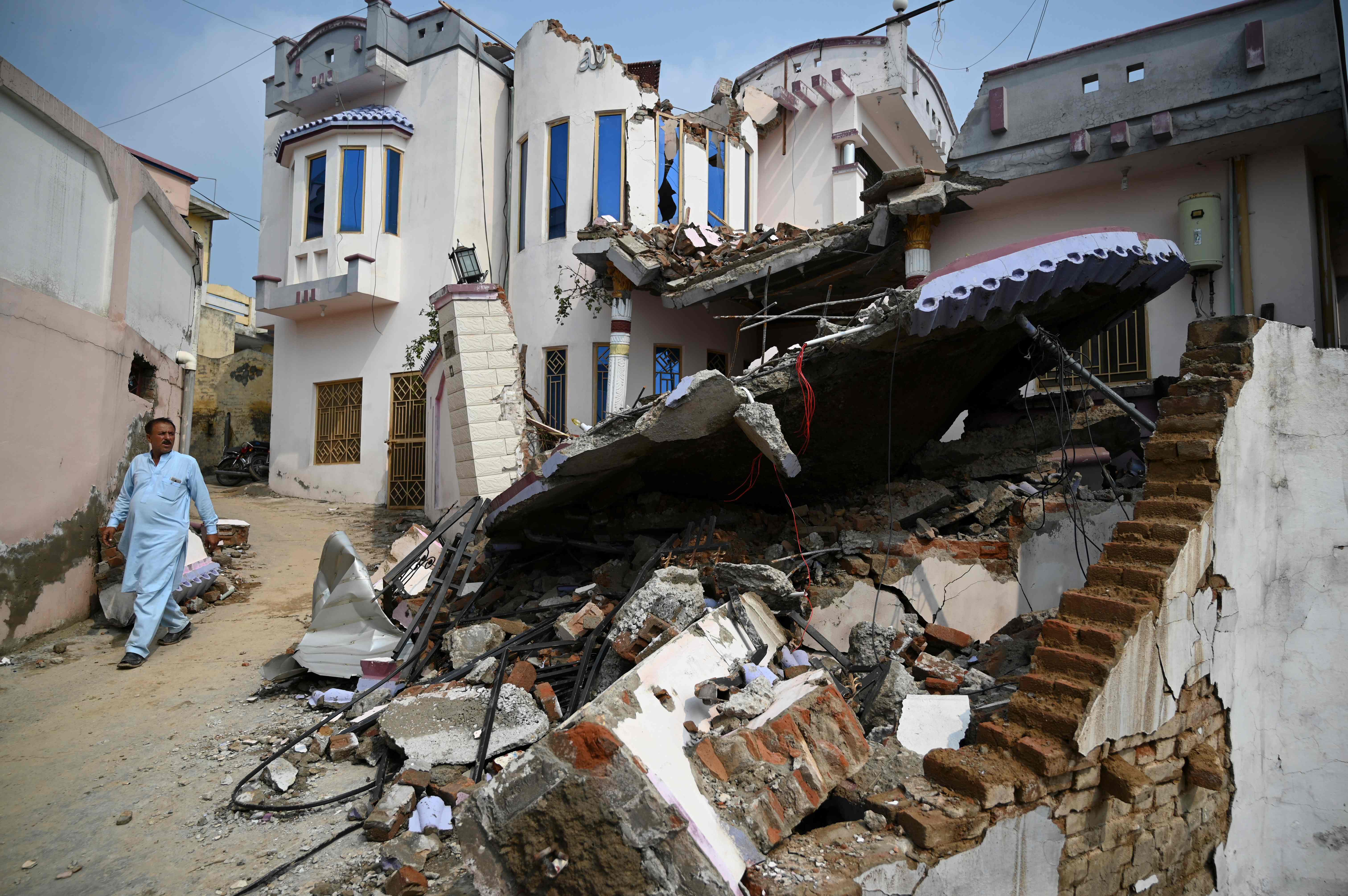 A Pakistani earthquake survivor walks past a collapsed house in an earthquake-hit area on the outskirts of Mirpur in Pakistan-controlled Kashmir on September 25, 2019. Rescuers battled along badly damaged roads and combed through toppled buildings September 25 to reach victims of an earthquake that killed at least 25 people and injured hundreds more in northeast Pakistan. (AFP)