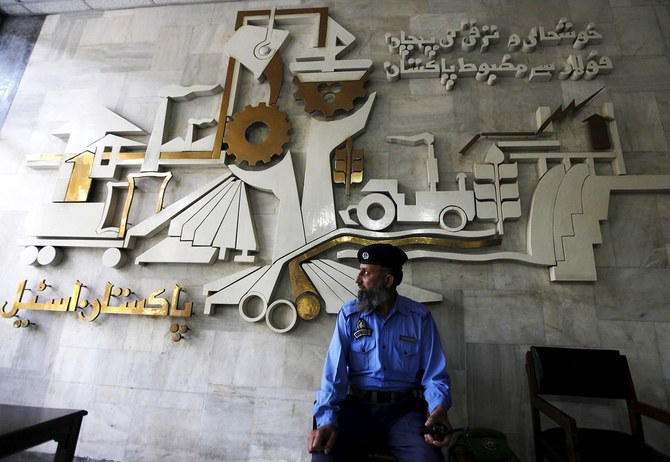 A security guard sits in front of a wall with signs and slogans at the operation building at the Pakistan Steel Mills (PSM) on the outskirts of Karachi Feb 8, 2016. (Reuters)