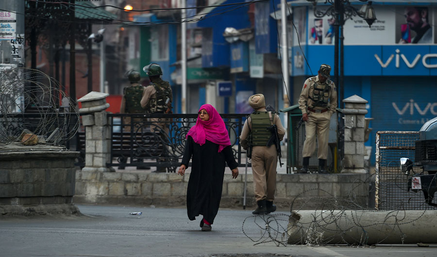 A Kashmiri woman walks as security personnel stand guard near a clock tower during a lockdown in central Srinagar on September 27, 2019. (AFP)