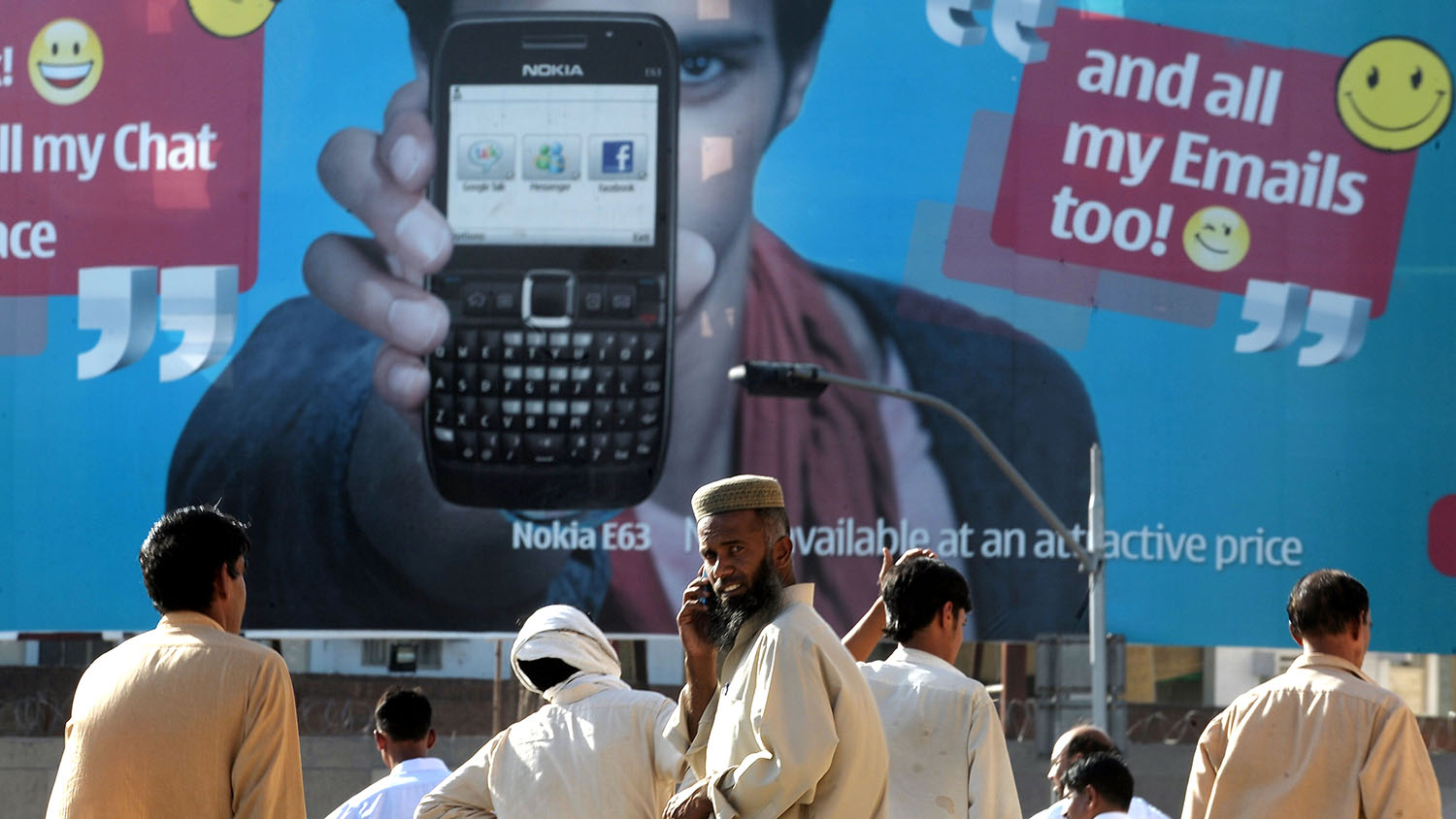 In this file photo, Pakistani pedestrians wait for transport as they stand in front of an advertisement for a cellular telephone in Rawalpindi on May 14, 2010. (AFP)