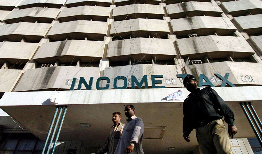Pakistani men walk in front of the income tax building in Karachi, 05 April 2005. (AFP)