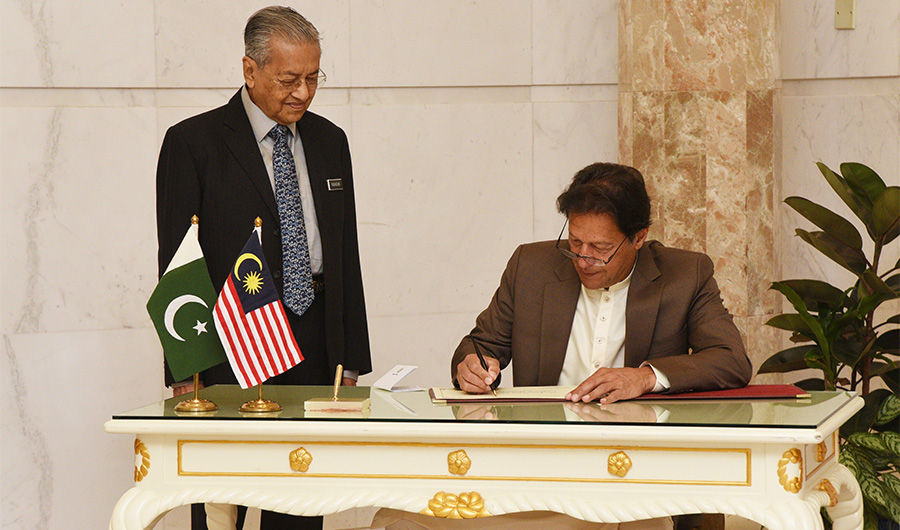 In this handout photo taken and released by Malaysia's Department of Information on February 4, 2020, Malaysia's Prime Minister Mahathir Mohamad (L) watches as Pakistan's Prime Minister Imran Khan signs a document during an official visit in Putrajaya. (AFP)