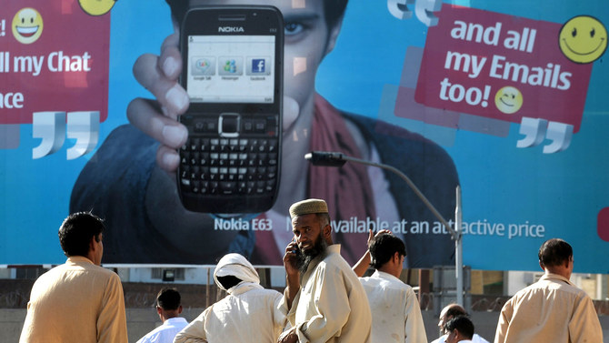 In this file photo, Pakistani pedestrians wait for transport as they stand in front of an advertisement for a cellular telephone in Rawalpindi on May 14, 2010. (AFP)