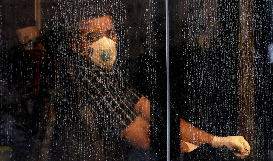 A commuter looks through a water-stained window wearing a mask and gloves to help guard against the Coronavirus, on a public bus in downtown Tehran, Iran, Sunday, Feb. 23, 2020. (AP Photo)