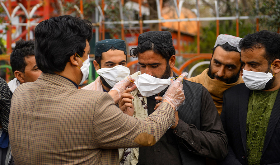 A volunteer, left, hands out free facemasks to people as a preventive measure against the spread of the coronavirus, in Herat city on Feb. 26, 2020. (AFP)