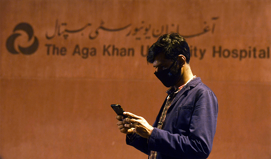 A Pakistani journalist wearing a protective facemask uses his mobile phone outside the Aga Khan University Hospital where a patient of the COVID-19 novel coronavirus has been admitted in Karachi on February 26, 2020. (AFP)