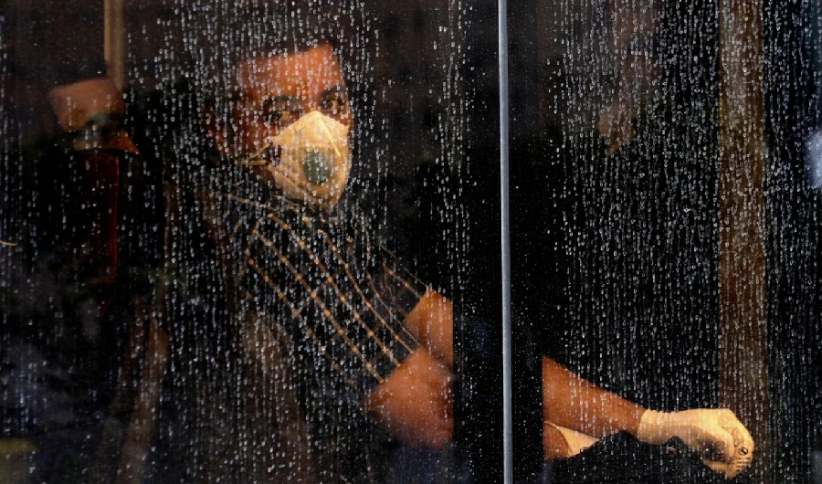 A commuter looks through a water-stained window wearing a mask and gloves to help guard against the Coronavirus, on a public bus in downtown Tehran, Iran, Sunday, Feb. 23, 2020. (AP Photo)