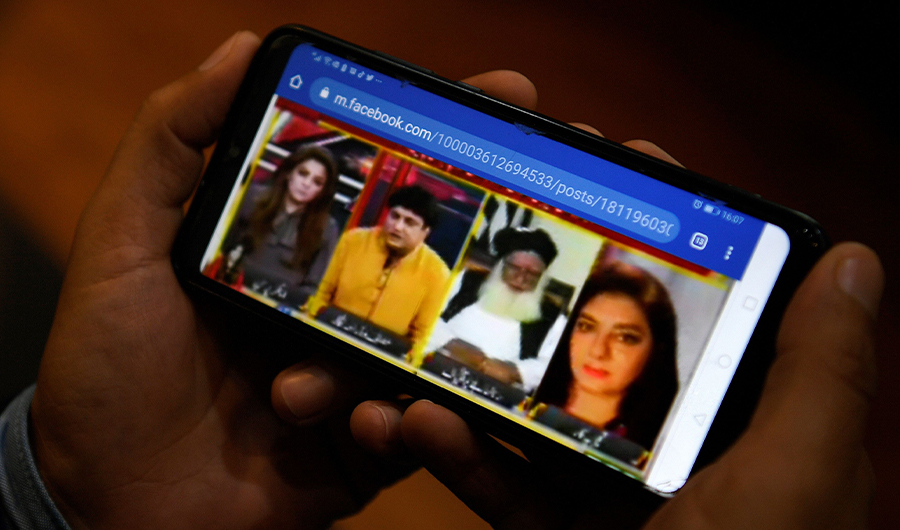 In this picture taken on March 5, 2020 a man watches a video clip on his mobile phone from a local TV channel about a debate on International Women Day's march between women rights activist Marvi Sirmed (R) and television play writer Khalil ur Rehman (2L), in Islamabad.