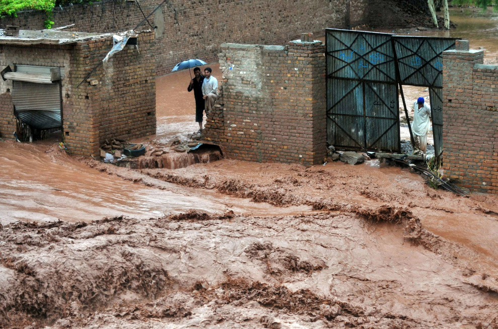 Residents watch water pour through a street on the outskirts of Peshawar, Pakistan on July 28, 2010. (AFP)
