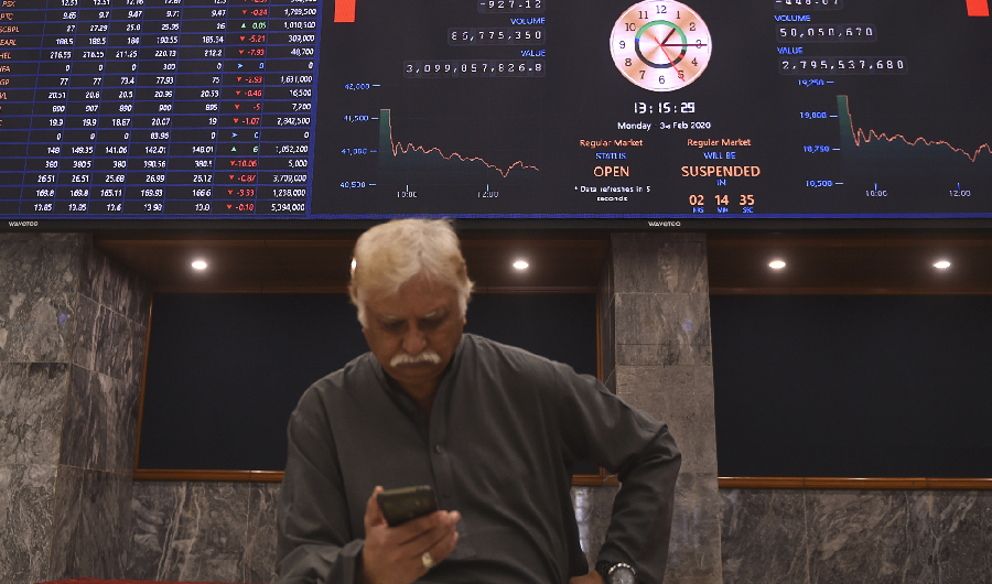 A stockbroker uses his phone beside an index board showing latest share prices during a trading session at the Pakistan Stock Exchange (PSX) in Karachi on February 3, 2020. (AFP)