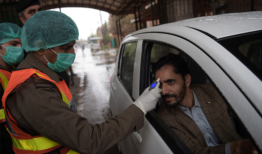 A health official of the Khyber Pakhtunkhwa emergency rescue service checks the body temperature of a government employee, as a preventive measure against the spread of the COVID-19 coronavirus, before entering their offices in Peshawar on March 12, 2020. (AFP)