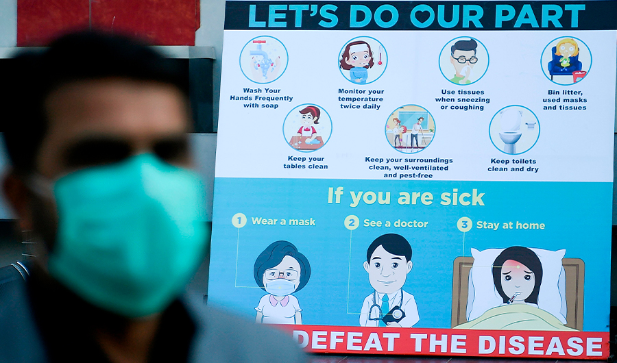 A man wearing a facemask walks past a sign board displaying preventive meausres against the spread of the COVID-19 novel coronavirus, outside a mall in Islamabad on March 16, 2020. (AFP)