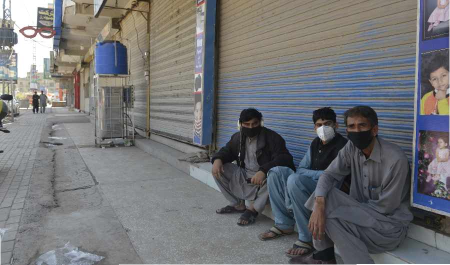 Shopkeepers wearing facemask sit in front of closed shops of a market area in Rawalpindi on March 22, 2020, after Punjab Province government announced the closing of shops and markets amid concerns over the spread of the COVID-19 novel coronavirus. (AFP)