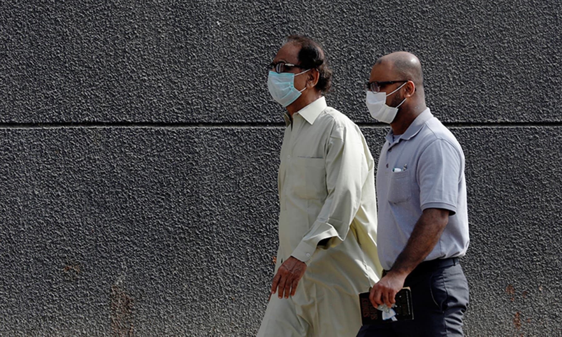 Men walk with face masks as a preventive measure, after Pakistan confirmed its first two cases of coronavirus, along a sidewalk in Karachi, Pakistan February 28, 2020. (REUTERS)