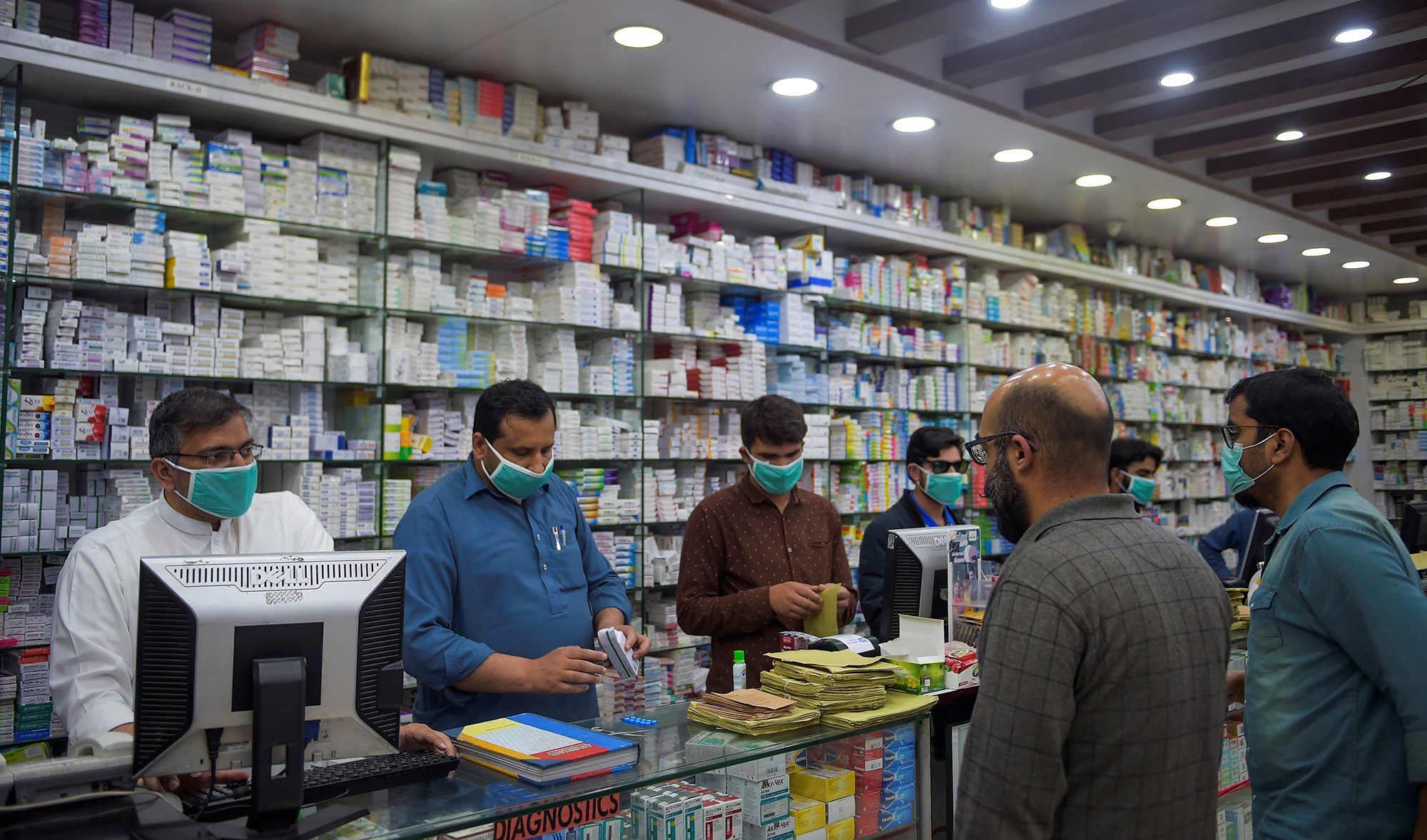 Pharmacy employees wearing facemasks as a preventive measure against the COVID-19 coronavirus attend to customers in Islamabad on March 23, 2020. (AFP)