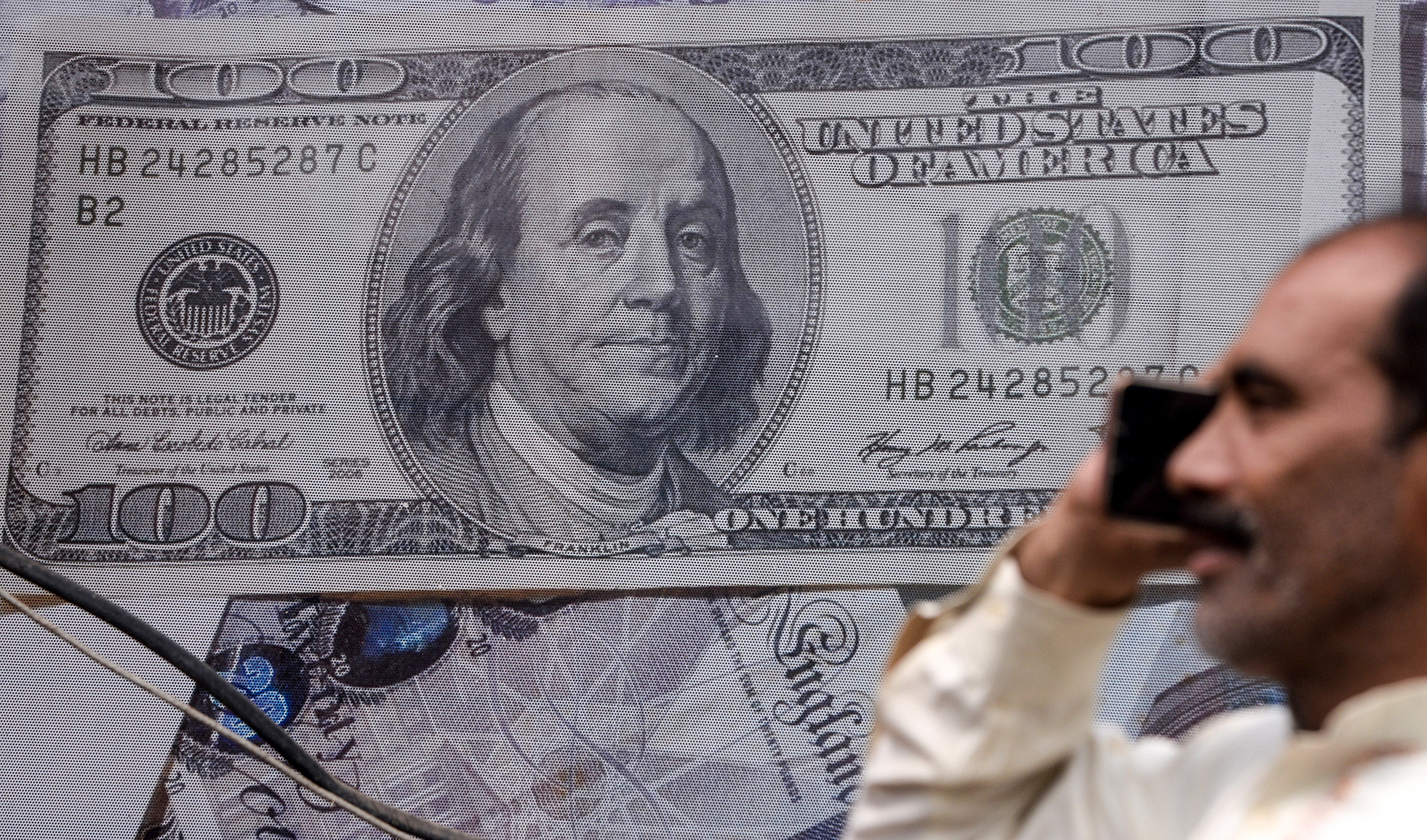 In this file photo, a Pakistani man talks on the phone in front of a poster displaying US dollars at the currency exchange place in Lahore on May 16, 2019. (AFP)