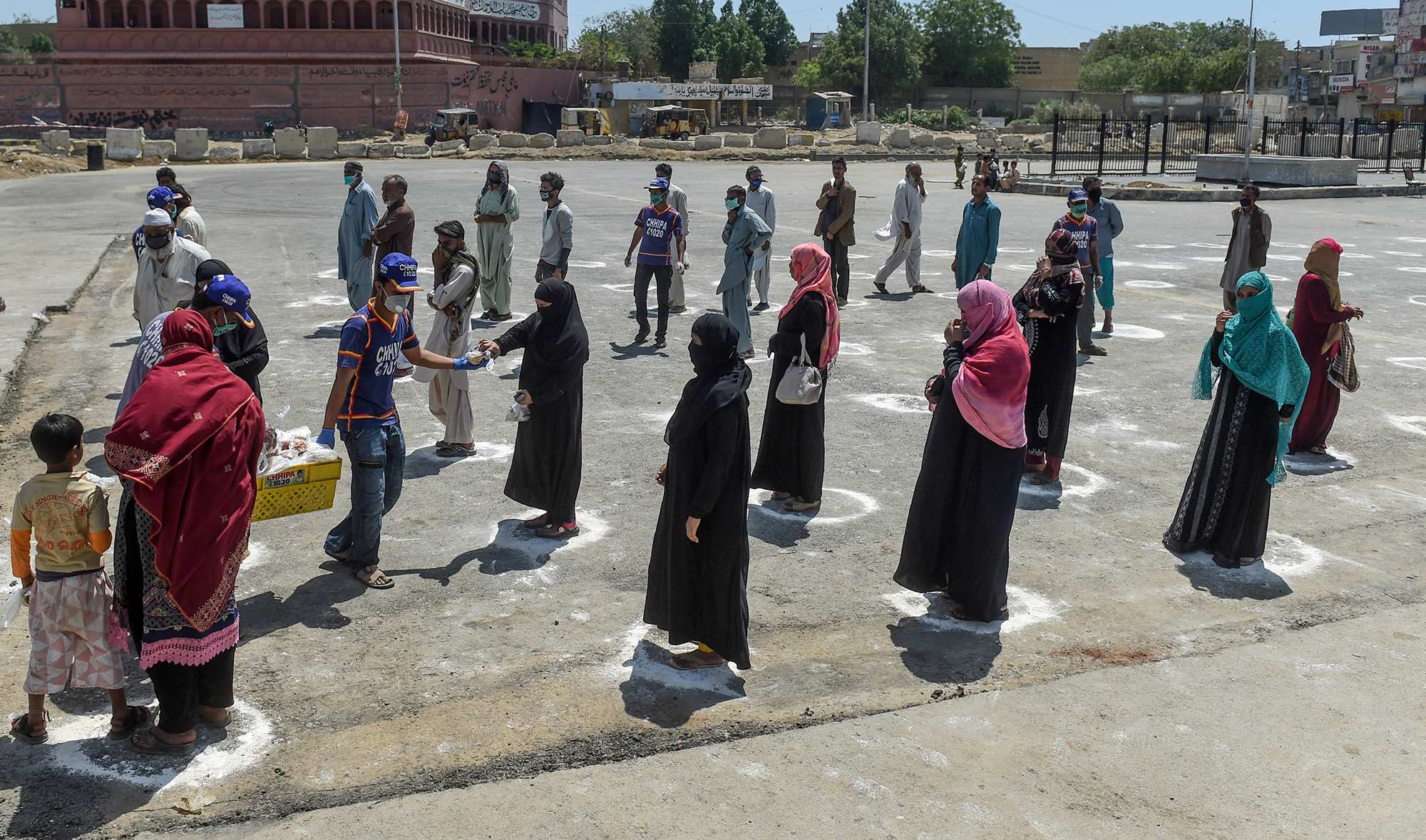 People stand in designated areas marked on the ground to maintain social distanciation as they receive free food from volunteers of Chhipa Welfare Association during a government-imposed nationwide lockdown as a preventive measure against the COVID-19 coronavirus in Karachi on March 27, 2020. (AFP)