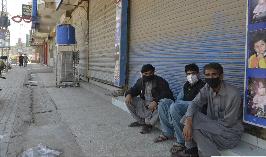 Shopkeepers wearing facemask sit in front of closed shops of a market area in Rawalpindi on March 22, 2020, after Punjab Province government announced the closing of shops and markets amid concerns over the spread of the COVID-19 novel coronavirus. (AFP)