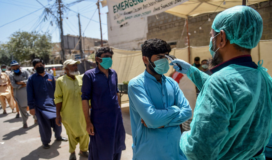 A municipal worker (R) checks the body temperature of a man queuing along with other people at a low-rate food distribution point during a government-imposed nationwide lockdown as a preventive measure against the COVID-19 coronavirus, in Karachi on April 4, 2020. (AFP)