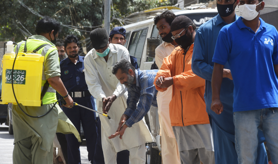 A worker sprays sanitiser on the hands of man lining up maintaining social distancing to buy groceries from a governmental subsidised shop during a government-imposed nationwide lockdown as a preventive measure against the spread of the COVID-19 coronavirus, in Karachi on April 8, 2020. (AFP)