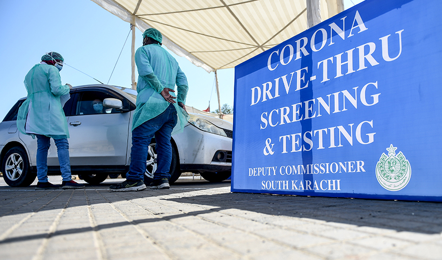 Medical staff members wearing protective gear take information from a resident sitting in a car for a coronavirus test at a drive-through screening and testing facility point during a government-imposed nationwide lockdown as a preventive measure against the COVID-19 coronavirus, at the port city of Karachi on April 4, 2020. (AFP)