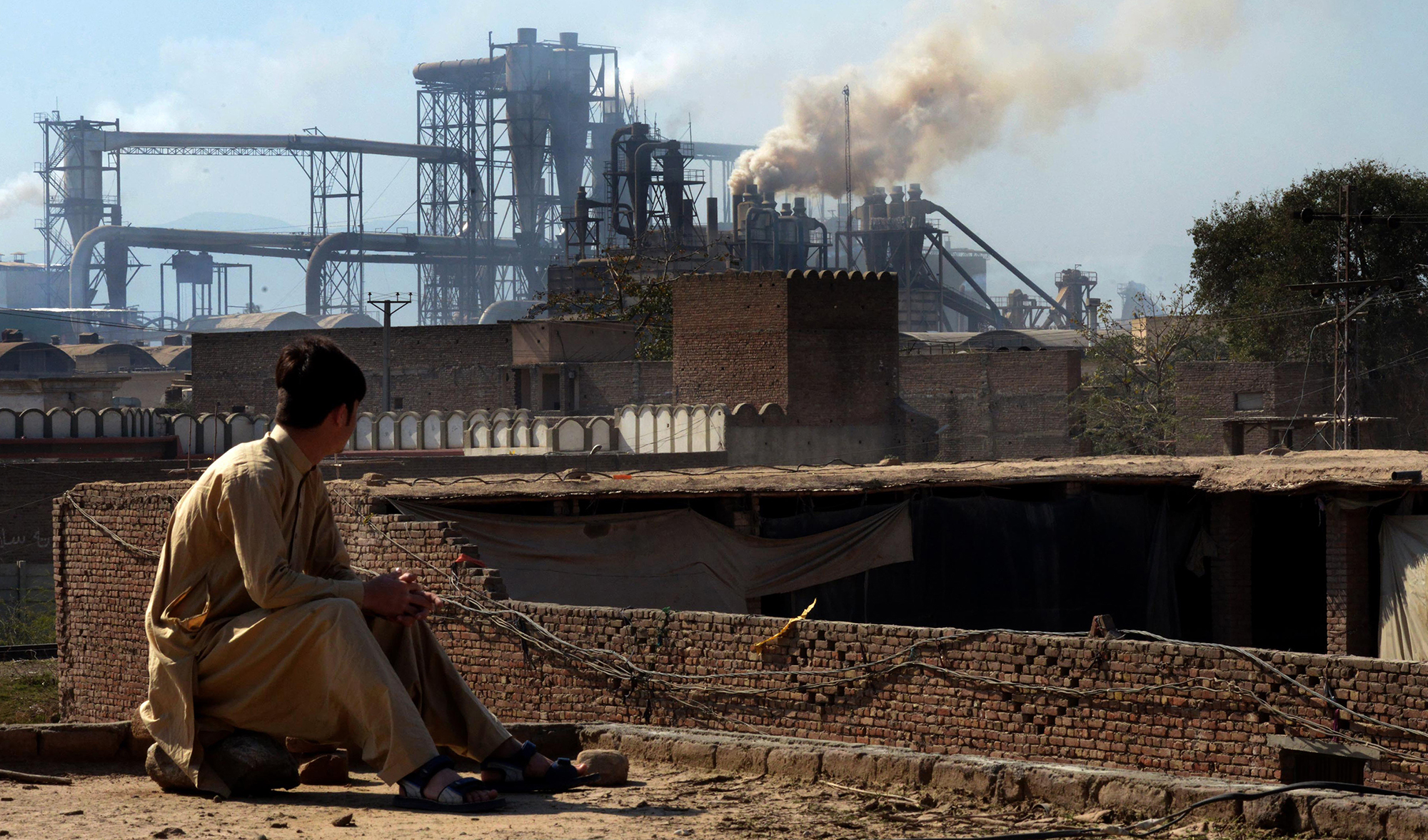 This file photo shows a Pakistani worker watching smoke rising from factories on the outskirts of the northwestern city of Peshawar on Feb. 25, 2017. (AFP)