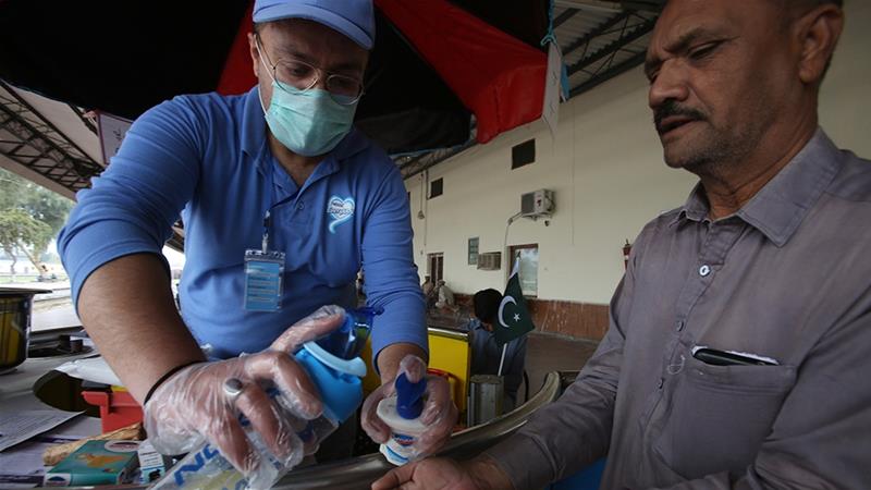 A volunteer helps a passenger arriving at a railway station to clean his hands to help prevent the spread of coronavirus in Peshawar. (AP)