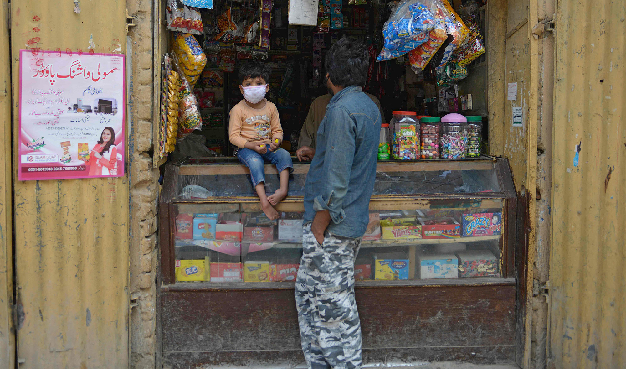 A man stands along with his son which wears a facemask at a shop during a government-imposed nationwide lockdown as a preventive measure against the COVID-19 coronavirus, in Rawalpindi on April 13, 2020. (AFP)