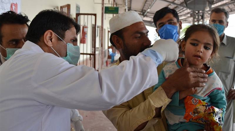 A man holds his daughter at Peshawar Railway Station as a health official checks her temperature amid concerns over the spread of COVID-19. (AFP)