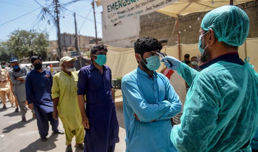 A municipal worker (R) checks the body temperature of a man queuing along with other people at a low-rate food distribution point during a government-imposed nationwide lockdown as a preventive measure against the COVID-19 coronavirus, in Karachi on April 4, 2020. (AFP)