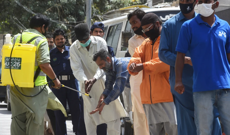 A worker sprays sanitiser on the hands of man lining up maintaining social distancing to buy groceries from a governmental subsidised shop during a government-imposed nationwide lockdown as a preventive measure against the spread of the COVID-19 coronavirus, in Karachi on April 8, 2020. (AFP)