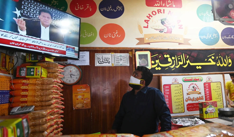 A bread maker wearing a facemask watches on television Pakistan's Prime Minister Imran Khan (L top) addressing to the nation during a government-imposed nationwide lockdown as a preventive measure against the COVID-19 coronavirus, in Islamabad on April 14, 2020. (AFP)