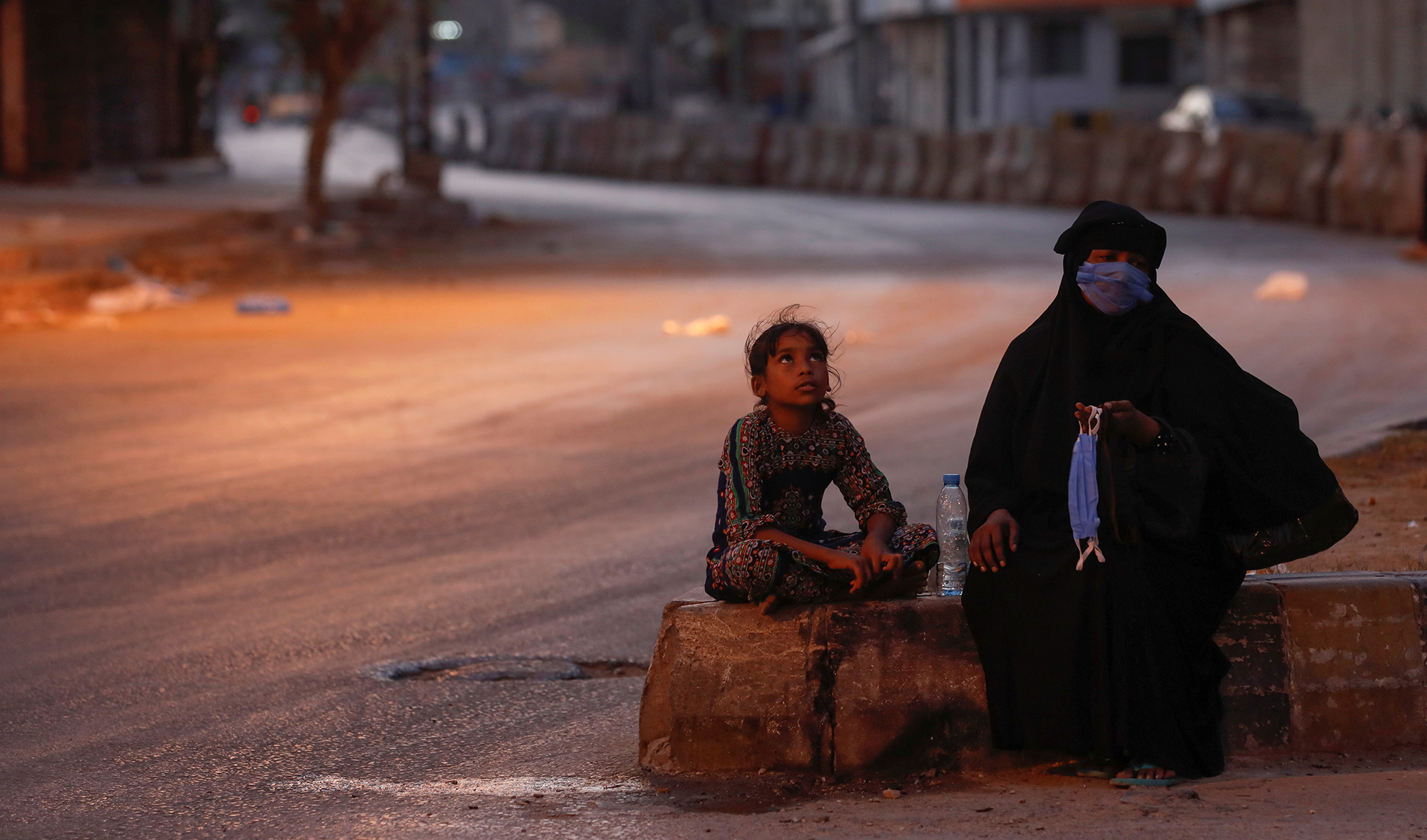 A woman and a girl sit on a deserted road as they sell handmade masks amid lockdown in Karachi, April 28, 2020. (REUTERS)