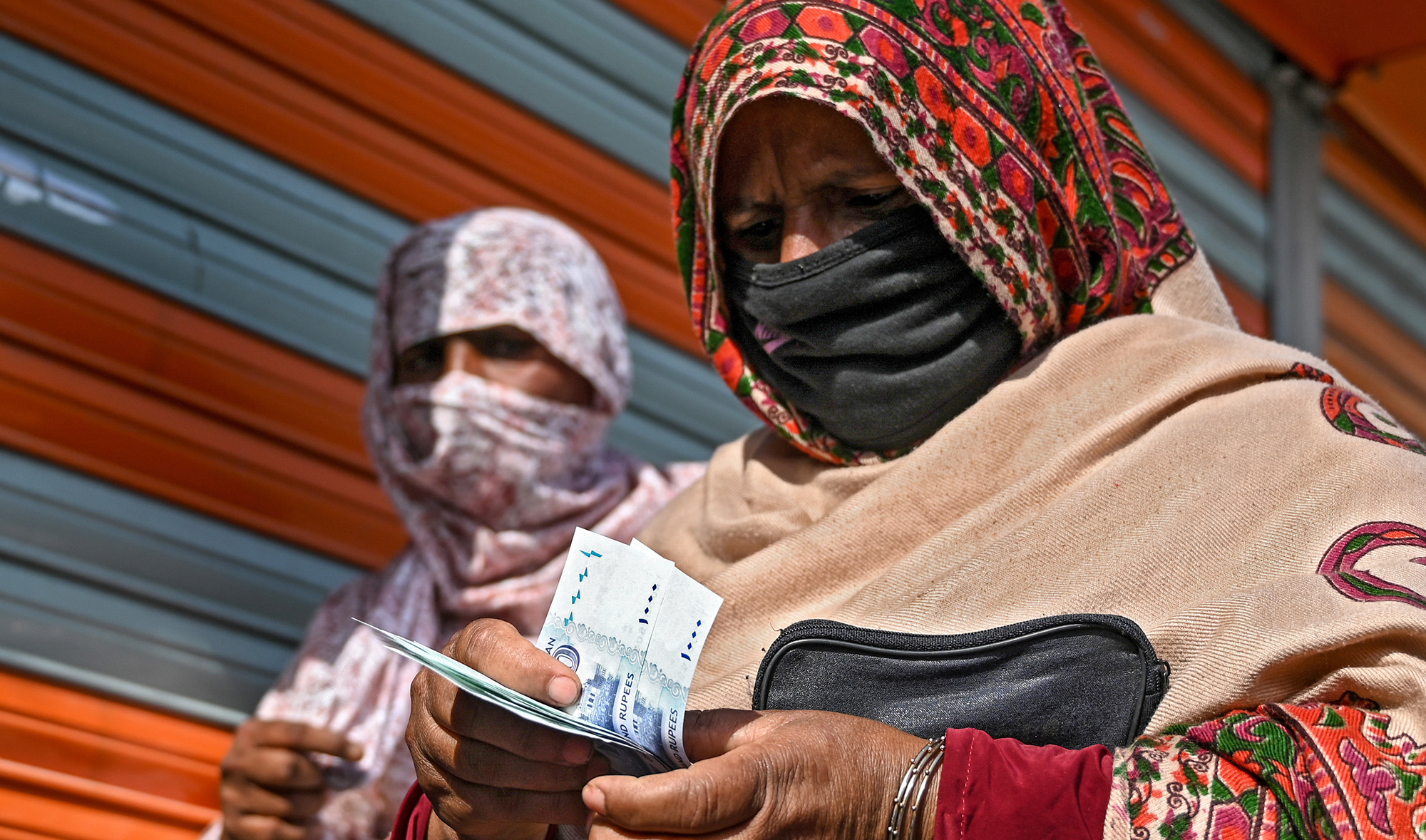 In this file photo, a woman in a face mask counts rupee notes as she walks on a street in Islamabad on April 9, 2020. (AFP)