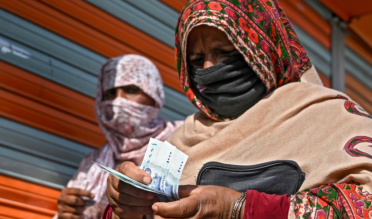 In this file photo, a woman in a face mask counts rupee notes as she walks on a street in Islamabad on April 9, 2020. (AFP)