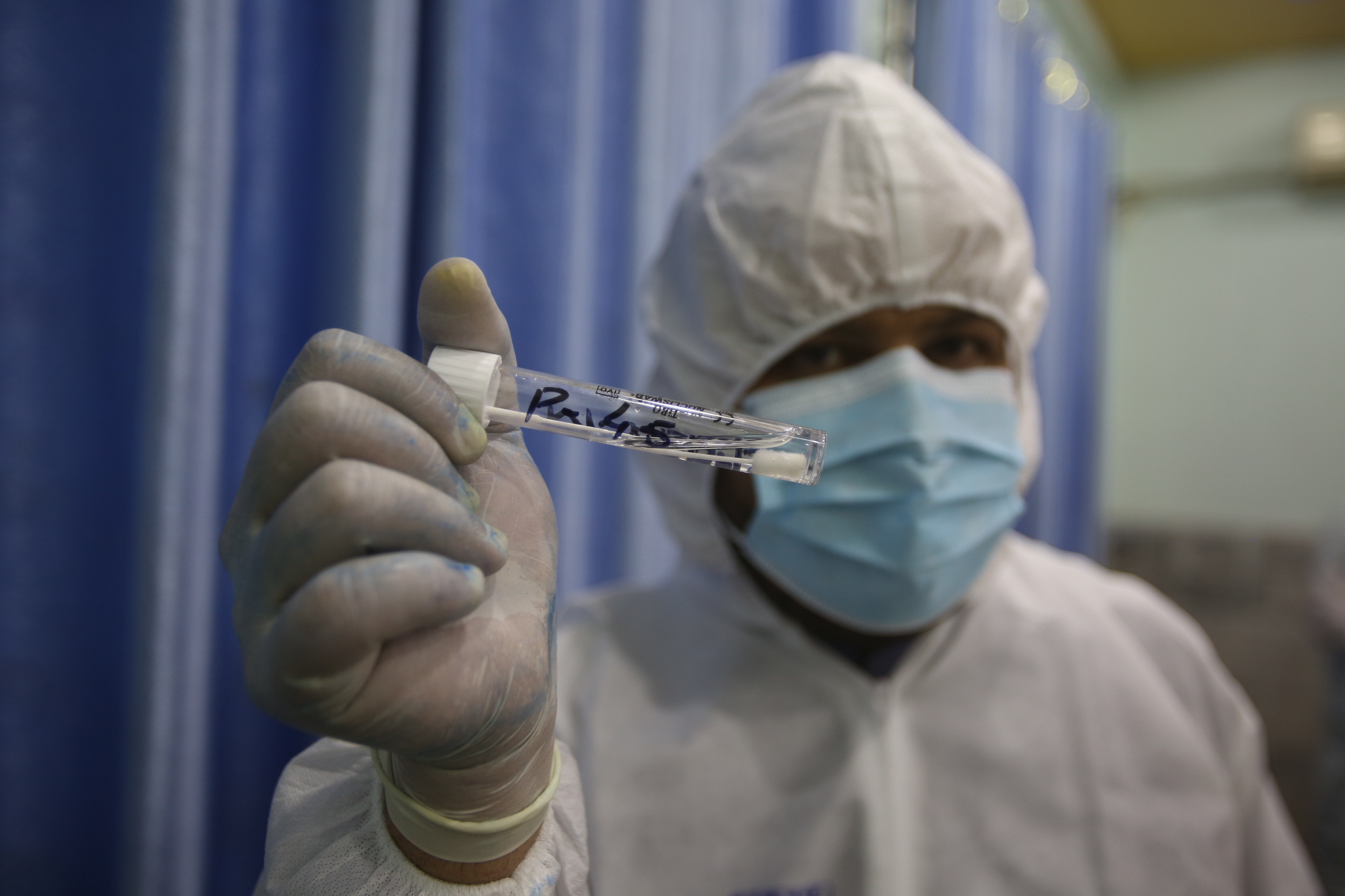 A health official in protective gear holds sample collected from a man at a screening and testing facility for COVID-19 in Peshawar, Pakistan, Wednesday, June 3, 2020. (AP)