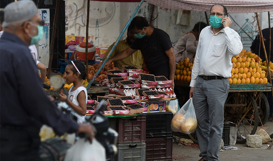 People wearing facemasks buy fruit alongside a street in Karachi on June 2, 2020. (AFP)