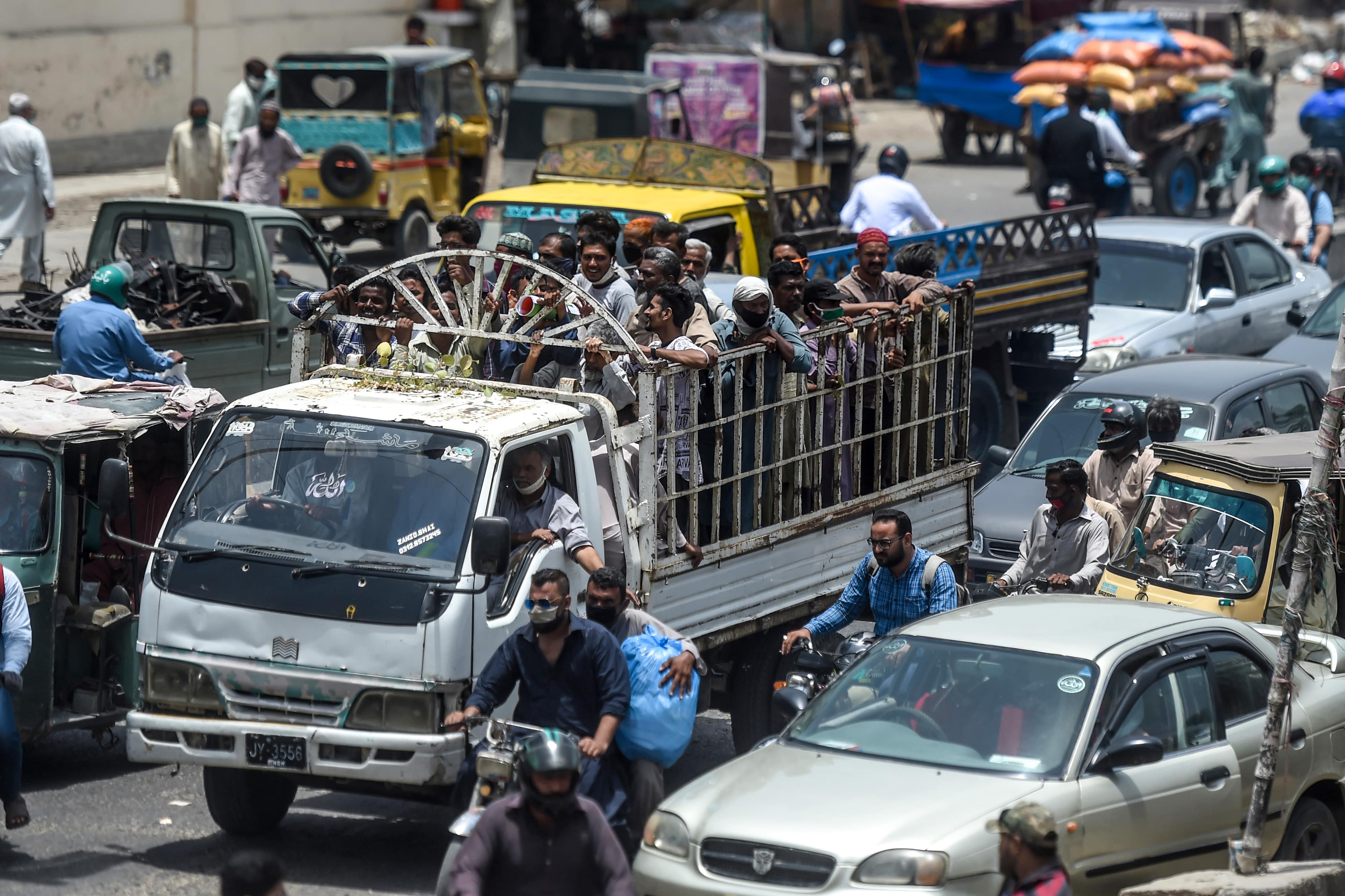 People ride on the back of a mini truck (C) after the government resumed public transport services easing the lockdown imposed against the COVID-19 coronavirus, in Pakistan's port city of Karachi on June 3, 2020. (AFP)