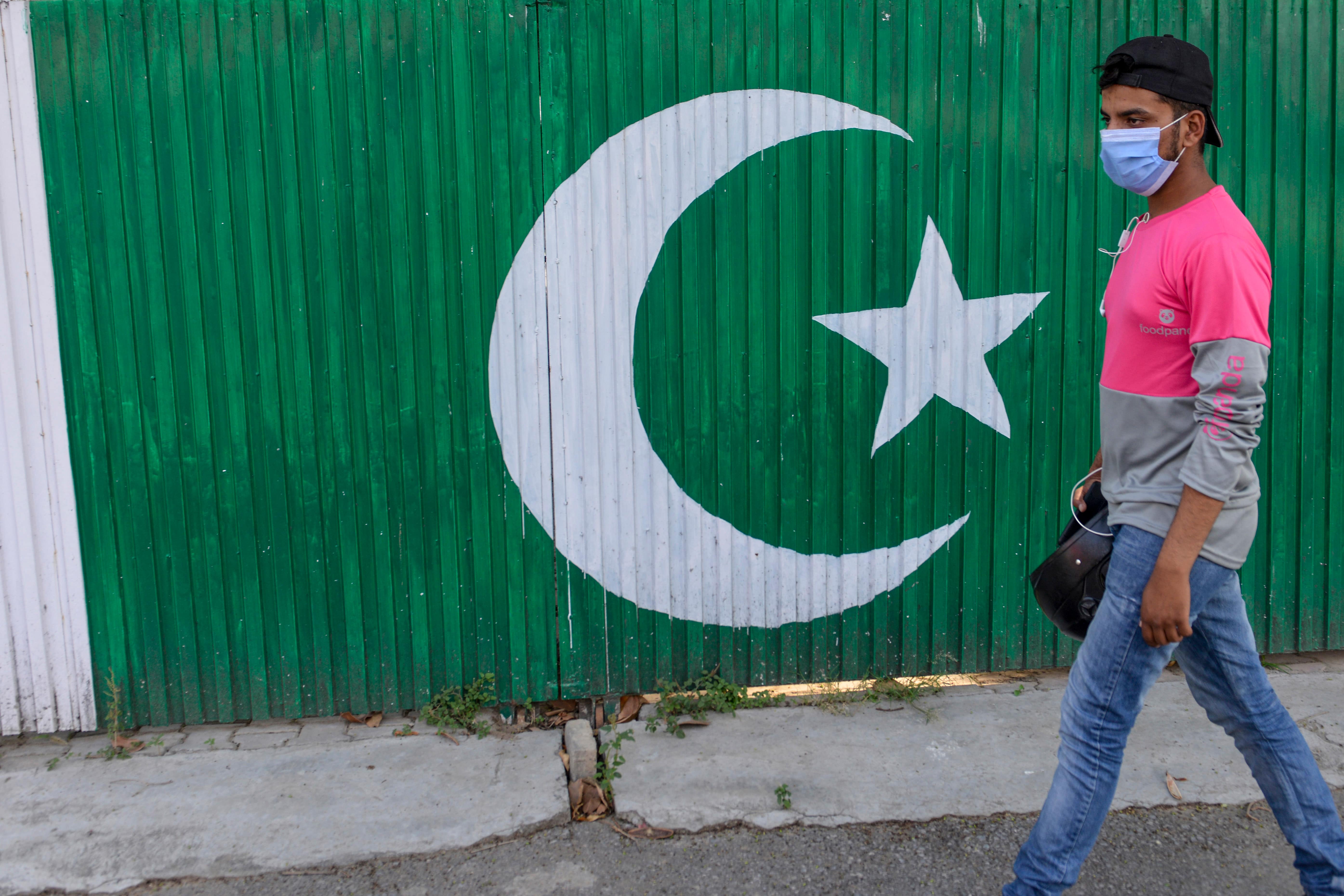 A food delivery boy walks past a hotel gate painted with Pakistan's national flag on a street in Rawalpindi on June 6, 2020. (AFP)