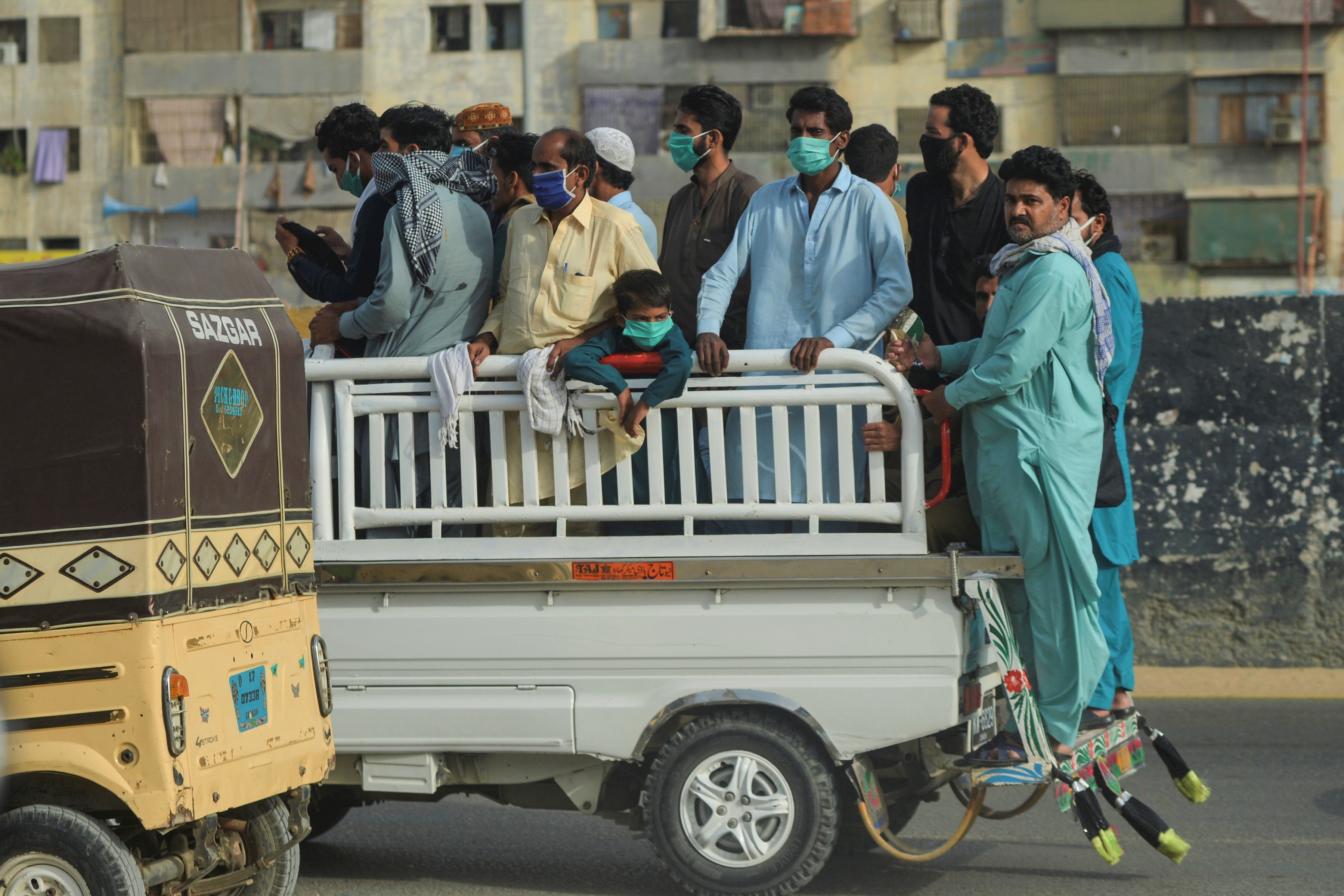 People ride on the back of a vehicle after the government resumed public transport services, in Pakistan's port city of Karachi on June 3, 2020. (AFP)