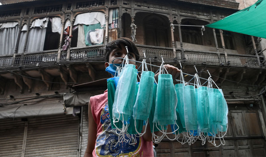 A young vendor sells facemasks on a street near a restricted area sealed by the authorities in Lahore on June 25, 2020, as COVID-19 coronavirus cases continue to rise. (AFP)