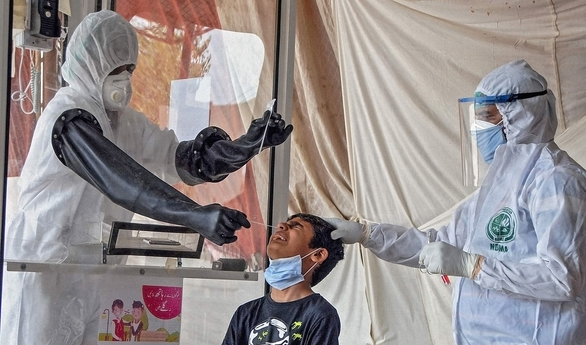 Health officials wearing protective gear take a nasal swab sample from a young boy, center, at a screening and testing facility for the COVID-19 coronavirus, in Hyderabad, Pakistan on June 26, 2020. (AFP)