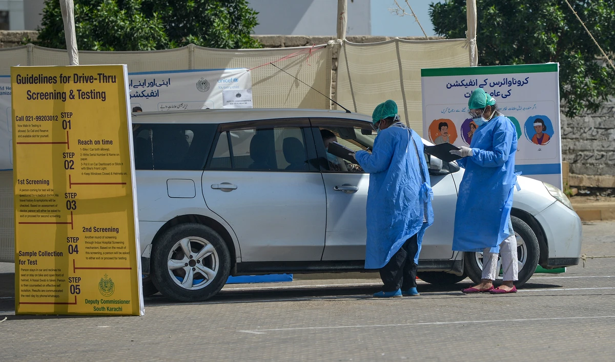 In this file photo, medical staff members wearing protective gear take information from a resident sitting in a car for a coronavirus test at a drive-through screening and testing facility point during a government-imposed nationwide lockdown as a preventive measure against the COVID-19 coronavirus, at the port city of Karachi on April 4, 2020. (AFP)