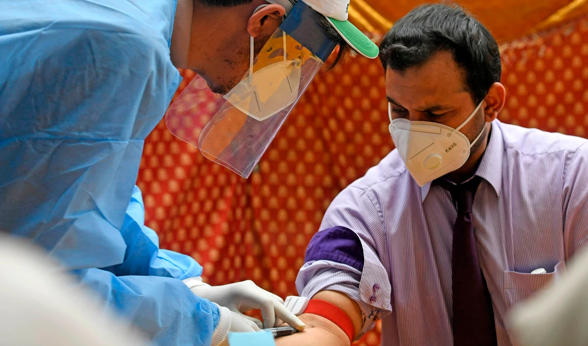 A health official wearing protective gear takes blood sample of a man at a drive-through screening and testing facility for the COVID-19 coronavirus, alongside a street in Islamabad on June 10, 2020. (AFP)
