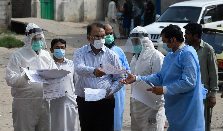 Health officials wearing Personal Protective Equipment (PPE) hold medical records collected form residents after taking samples for COVID-19 coronavirus during a door-to-door screening and testing operation at a slum area in Islamabad on June 30, 2020. (AFP)