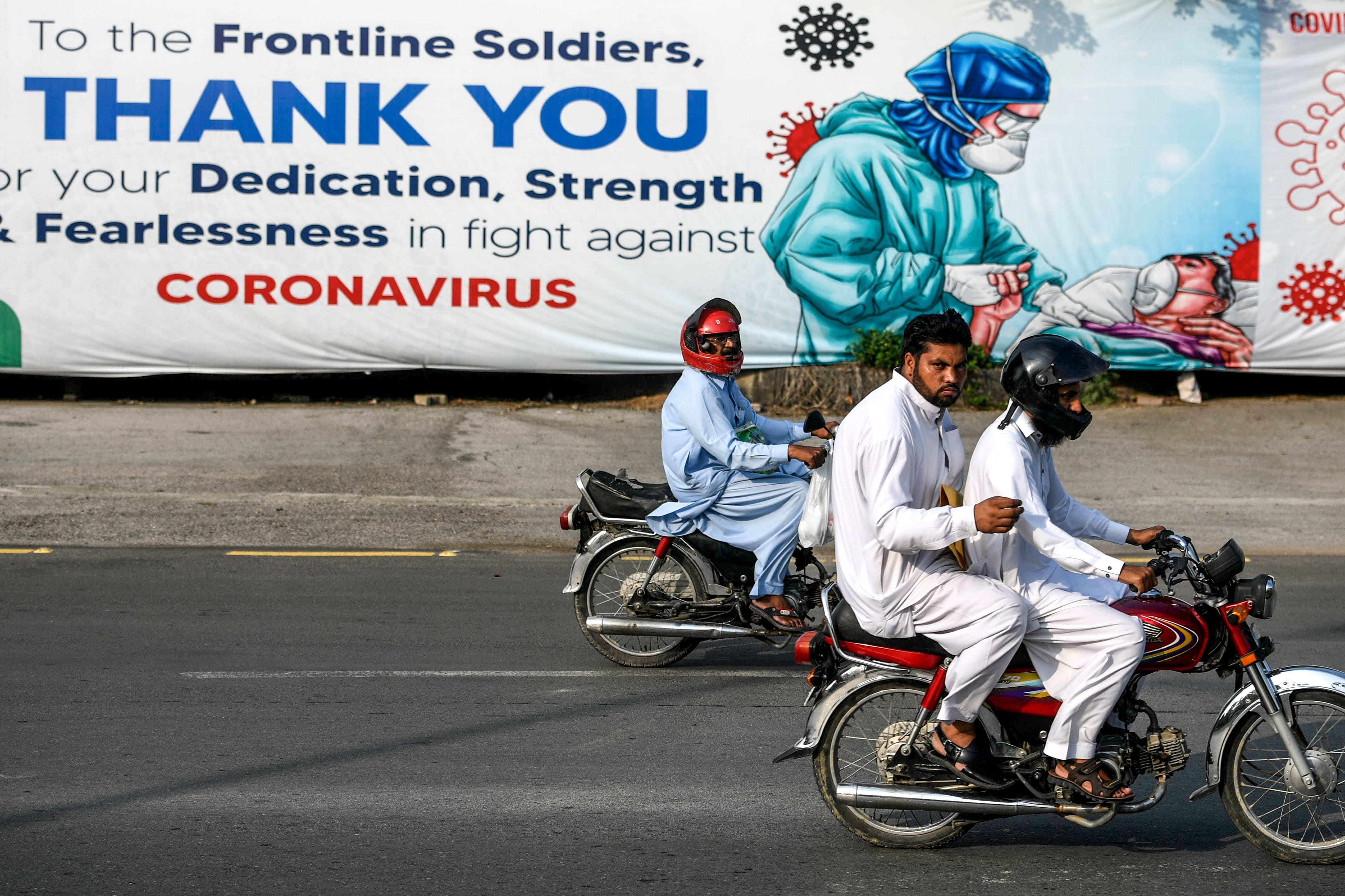 Motorcyclists ride past a banner paying tribute to health and medical workers for their fight against the COVID-19 coronavirus displayed on a street in Islamabad on July 8, 2020. (AFP)