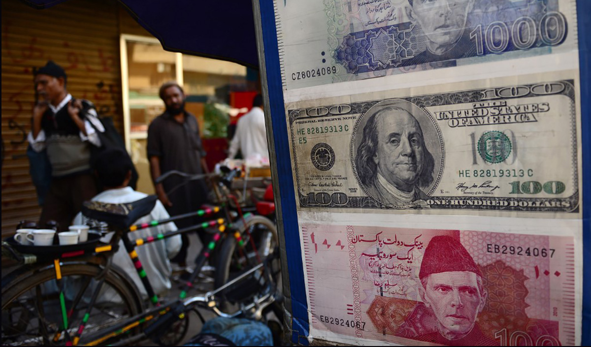 Pedestrians walk past a roadside currency exchange stall displaying examples of currency notes in Karachi on Feb. 11, 2013. (AFP/File)