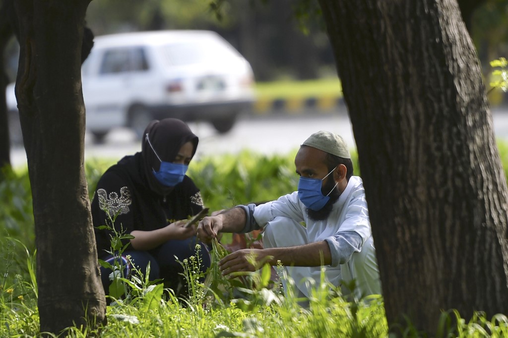 Local residents wearing face masks plant trees on a green belt along a street in Islamabad on March 13, 2020. Upon taking office in 2018, Imran Khan's government pledged to plant billions of trees to tackle the effects of climate change. (AFP)